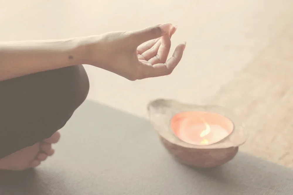 Hand in Meditationshaltung neben einer brennenden Kerze